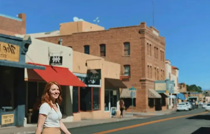 Smiling red-haired woman walking across a street in Old Town Scottsdale, surrounded by historic shops and buildings.
